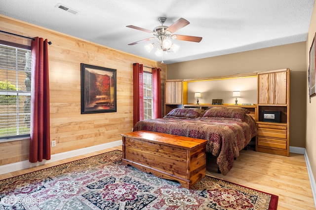 bedroom with wood walls, baseboards, light wood-style floors, and a ceiling fan