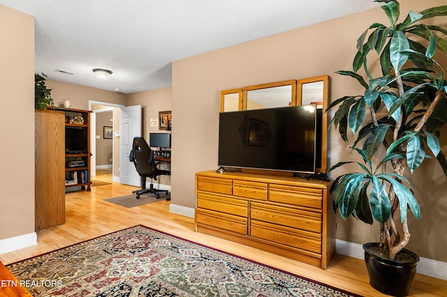 living area featuring light wood-style floors, a desk, and baseboards