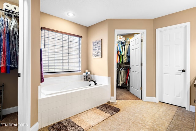 bathroom featuring a bath, baseboards, a spacious closet, and tile patterned flooring