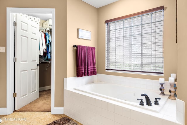 bathroom featuring tile patterned flooring, a walk in closet, a bath, and baseboards