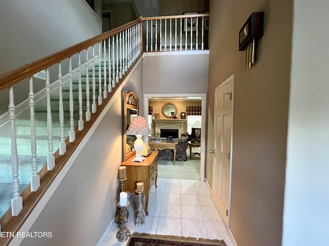 stairway with a high ceiling, a fireplace, tile patterned flooring, and baseboards