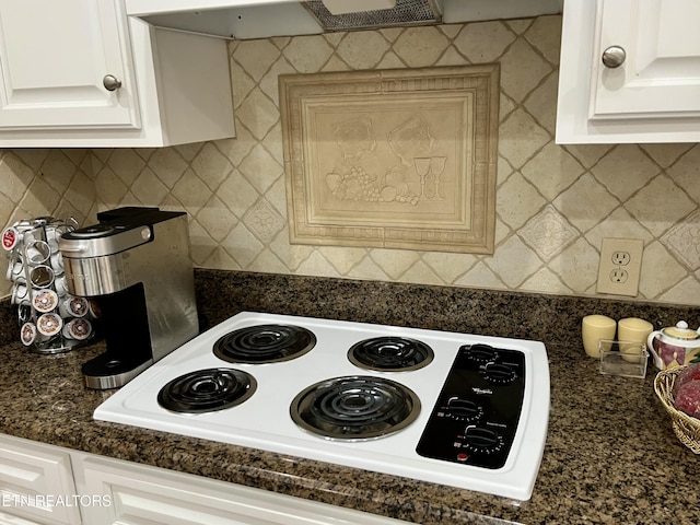 kitchen view of dark countertops, decorative backsplash, white electric stovetop, and white cabinets