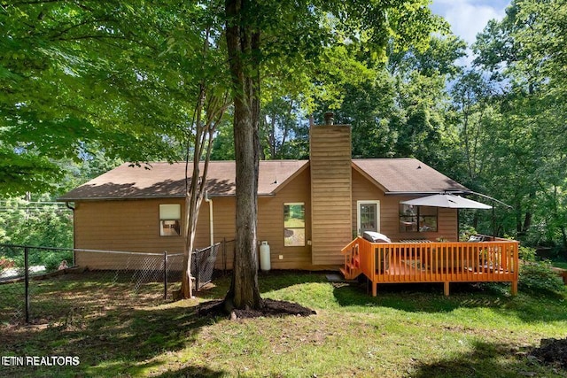 rear view of property featuring fence, a wooden deck, a chimney, and a lawn