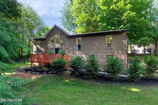 view of side of home featuring brick siding, a wooden deck, fence, and a lawn
