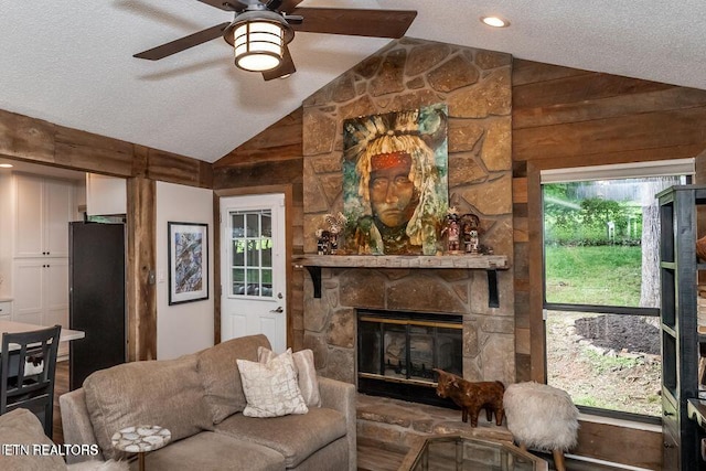 living room featuring a stone fireplace, a textured ceiling, vaulted ceiling, and ceiling fan