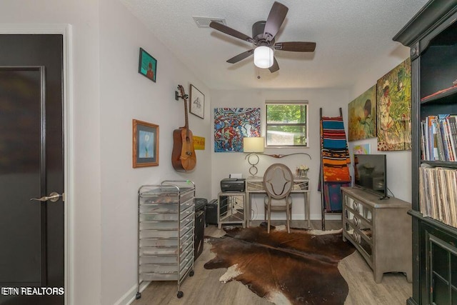 home office with wood finished floors, a ceiling fan, a textured ceiling, visible vents, and baseboards