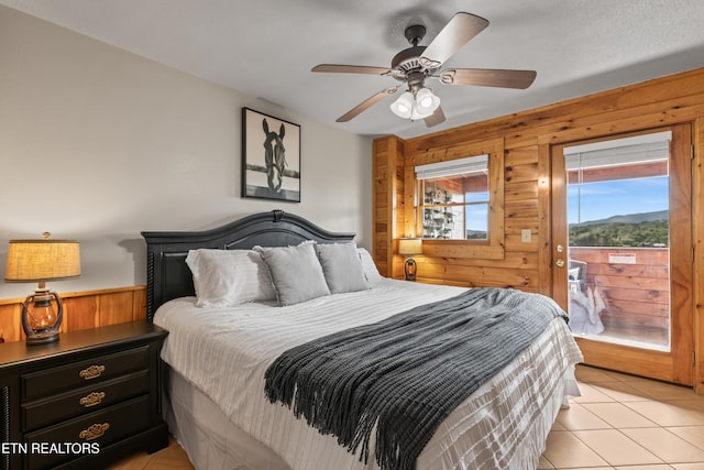 bedroom featuring wood walls, access to outside, light tile patterned floors, and a ceiling fan