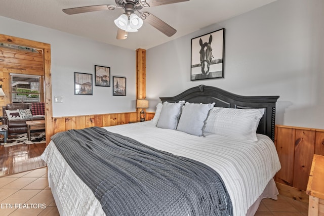 bedroom featuring light tile patterned floors, wood walls, a ceiling fan, and wainscoting