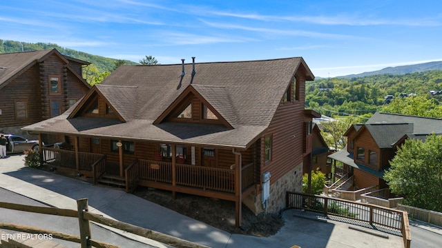 rear view of house featuring a mountain view, stone siding, covered porch, log siding, and roof with shingles