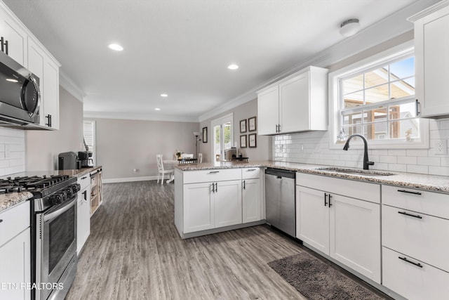 kitchen featuring appliances with stainless steel finishes, crown molding, a sink, a peninsula, and white cabinets