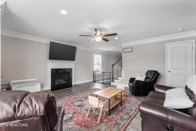 living area featuring ornamental molding, ceiling fan, stairs, wood finished floors, and a glass covered fireplace