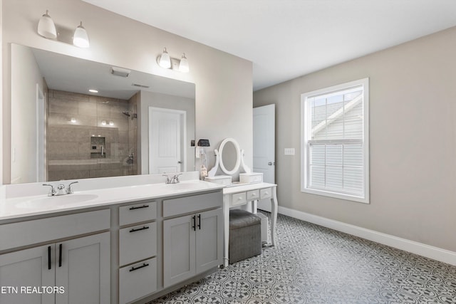bathroom featuring a tile shower, baseboards, and double vanity