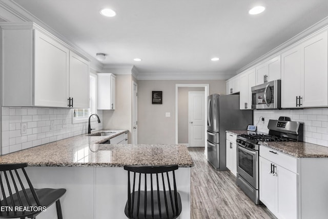 kitchen featuring stainless steel appliances, a sink, crown molding, white cabinetry, and light wood-style flooring