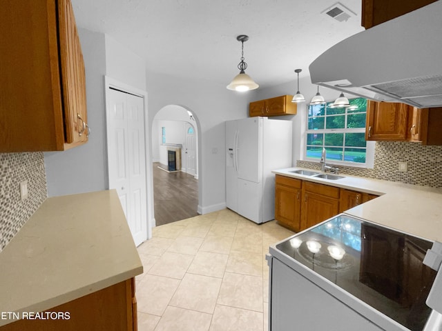kitchen with a sink, white appliances, decorative backsplash, arched walkways, and range hood