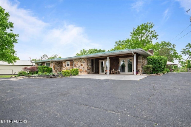 ranch-style house with metal roof, a chimney, french doors, and stone siding