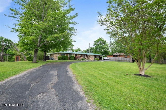 ranch-style home featuring a front lawn, fence, and aphalt driveway