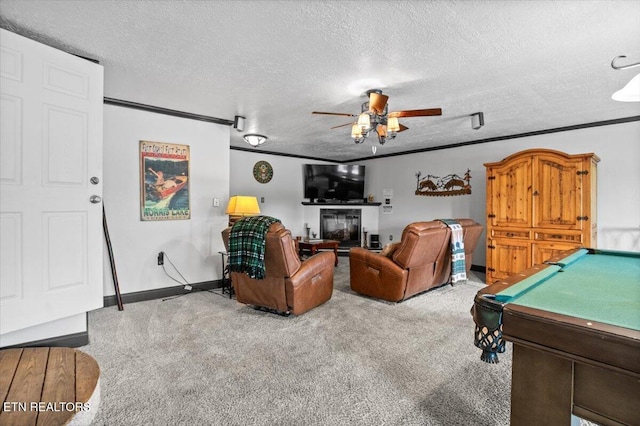 carpeted living room with a textured ceiling, pool table, ornamental molding, ceiling fan, and a glass covered fireplace