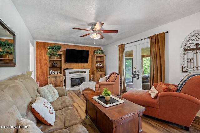 living area with a ceiling fan, french doors, a textured ceiling, a glass covered fireplace, and wood finished floors