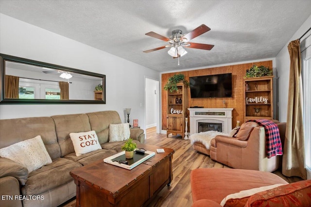 living area with a textured ceiling, baseboards, ceiling fan, a glass covered fireplace, and light wood-style floors