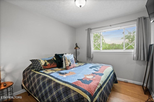 bedroom with a textured ceiling, baseboards, and wood finished floors