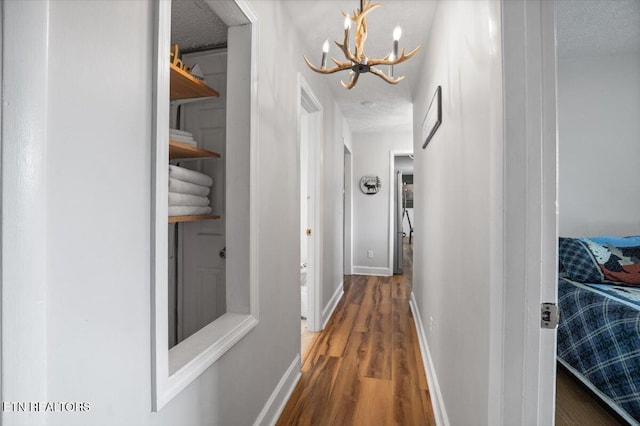 corridor with an inviting chandelier, a textured ceiling, baseboards, and wood finished floors