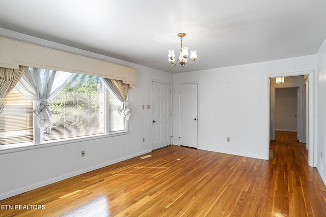 unfurnished room featuring a chandelier, light wood-type flooring, and baseboards