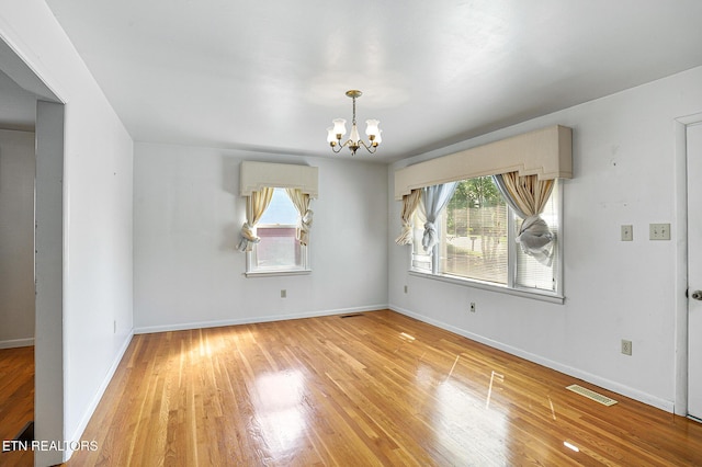 unfurnished dining area with healthy amount of natural light, a chandelier, light wood-style flooring, and baseboards