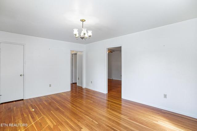 empty room with a chandelier, light wood-style floors, and baseboards