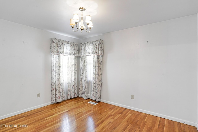 unfurnished room featuring a chandelier, baseboards, and wood finished floors