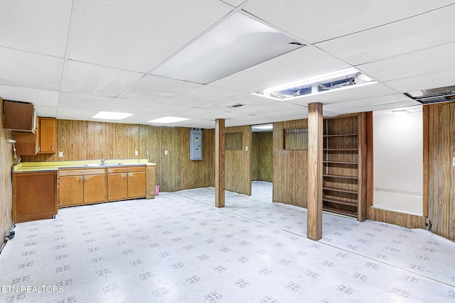 finished basement featuring wooden walls, a paneled ceiling, a sink, and electric panel
