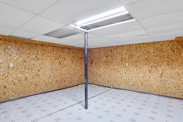 finished basement with a paneled ceiling, tile patterned floors, and wood walls