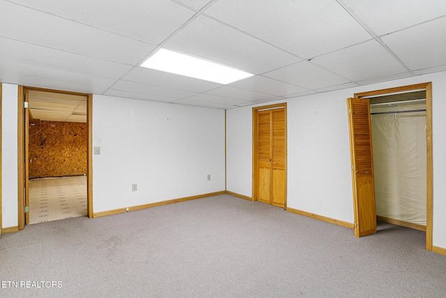 unfurnished bedroom with a drop ceiling, two closets, carpet, and baseboards