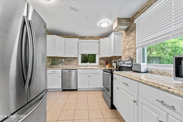 kitchen featuring stainless steel appliances, a sink, white cabinets, decorative backsplash, and light tile patterned flooring