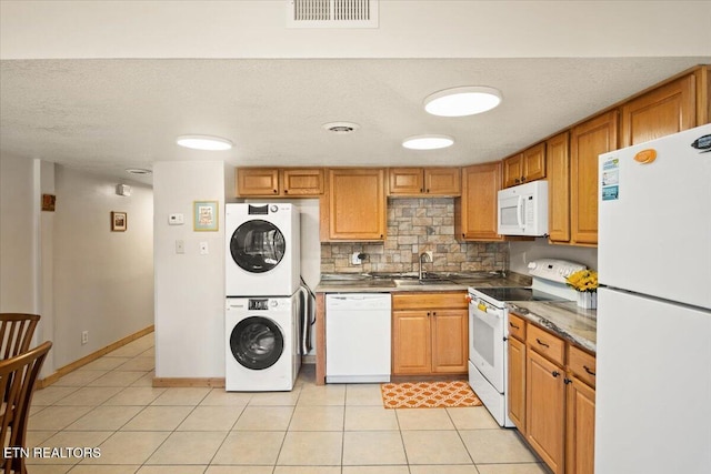 kitchen with white appliances, stacked washer / dryer, a sink, tasteful backsplash, and light tile patterned floors