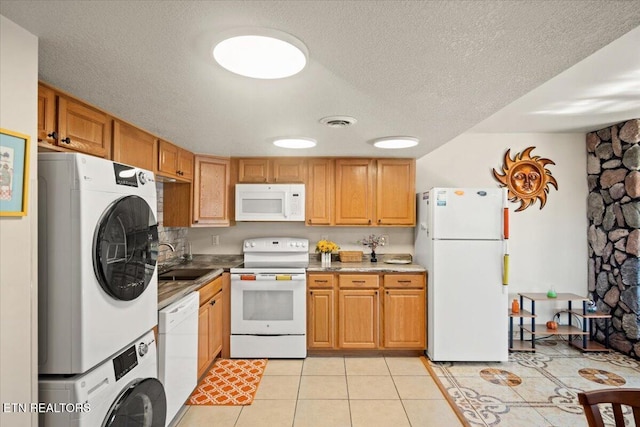 kitchen with white appliances, stacked washing machine and dryer, a sink, a textured ceiling, and light tile patterned floors