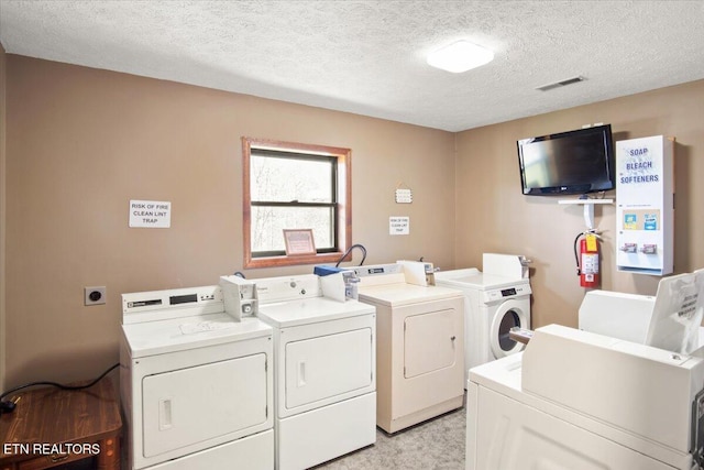 community laundry room with washer and clothes dryer, a textured ceiling, and light carpet