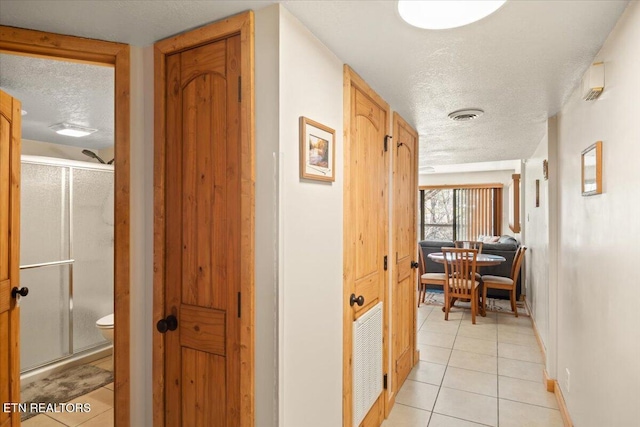 hallway with a textured ceiling, light tile patterned flooring, and baseboards