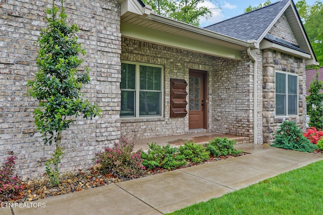 view of exterior entry featuring covered porch, brick siding, and a shingled roof
