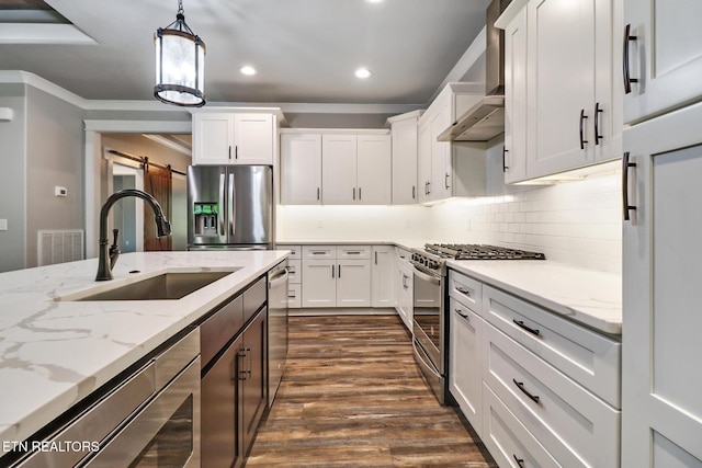 kitchen featuring stainless steel appliances, a barn door, wall chimney range hood, white cabinets, and crown molding