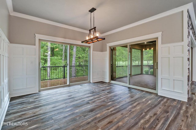 unfurnished dining area featuring a decorative wall, a chandelier, dark wood-style floors, plenty of natural light, and ornamental molding