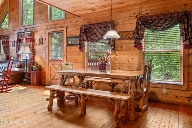 dining room featuring light wood-type flooring, healthy amount of natural light, wooden walls, and lofted ceiling
