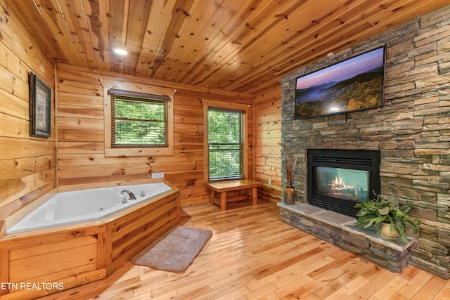 bathroom with a stone fireplace, a jetted tub, hardwood / wood-style floors, wooden ceiling, and wood walls