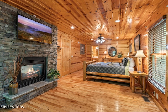 bedroom featuring hardwood / wood-style flooring, a stone fireplace, wooden ceiling, wood walls, and recessed lighting