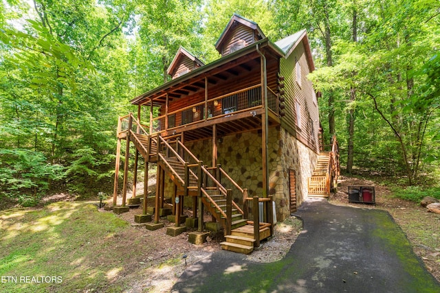 rear view of house featuring stairway, stone siding, a wooden deck, and a wooded view