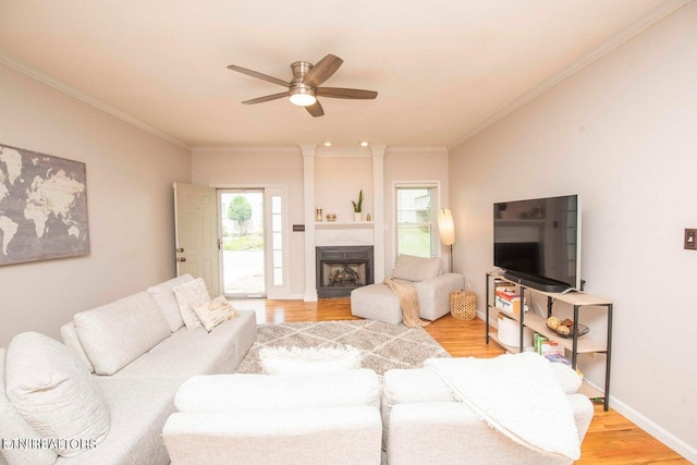 living area featuring light wood finished floors, a ceiling fan, crown molding, a fireplace, and baseboards