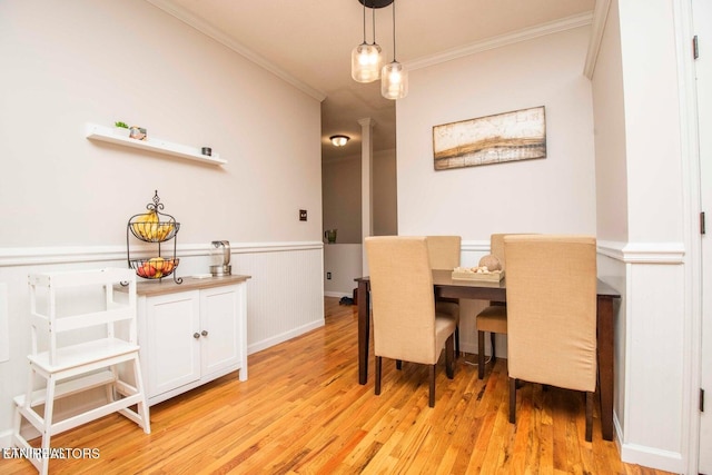dining area with crown molding, light wood-style floors, and wainscoting