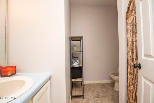 bathroom featuring vanity, toilet, stone finish floors, and baseboards