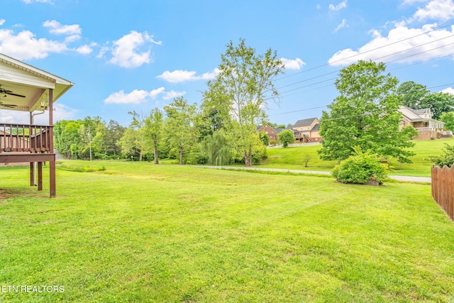 view of grassy yard featuring a ceiling fan and a deck