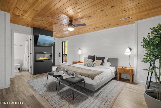 bedroom featuring wooden ceiling, wood finished floors, wooden walls, connected bathroom, and ceiling fan