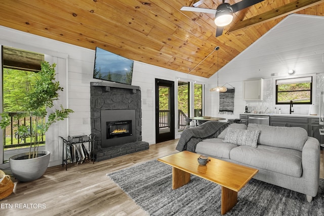 living room featuring healthy amount of natural light, a ceiling fan, a fireplace, wood finished floors, and wooden ceiling